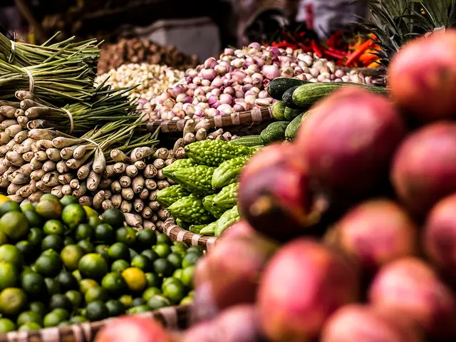 Close-up of a produce market stall piled with fresh lemongrass, garlic, bitter melon, limes, and pomegranates.