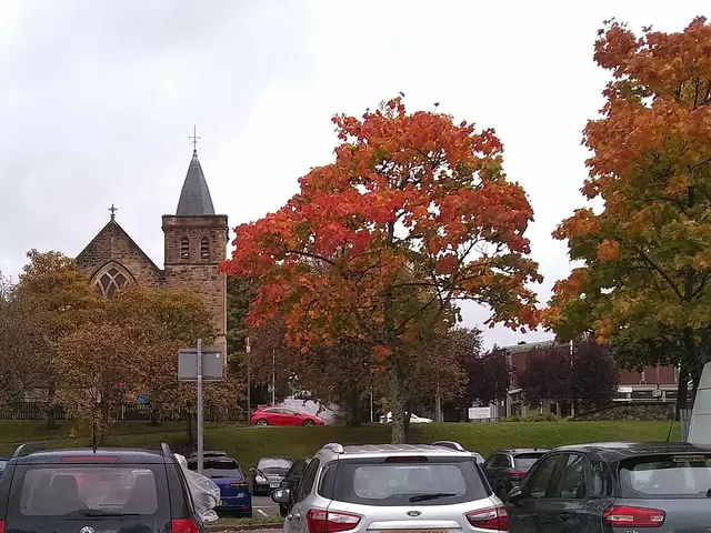 The exterior of a stone church building beside trees in autumn colour.