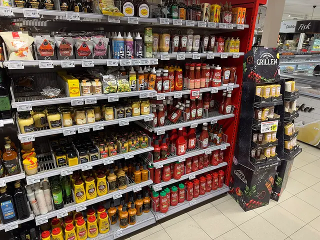 A grocery store aisle with shelves of condiments including mustard and ketchup, each with price tags.