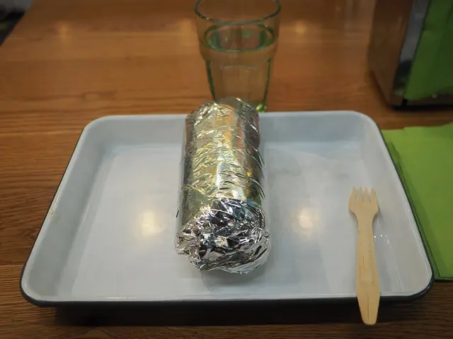 A burrito wrapped in aluminum foil at a restaurant.