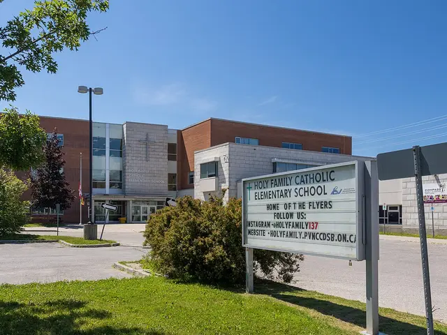The exterior of Holy Family Catholic Elementary School in Bowmanville, Ontario, with a cross and illuminated sign out front